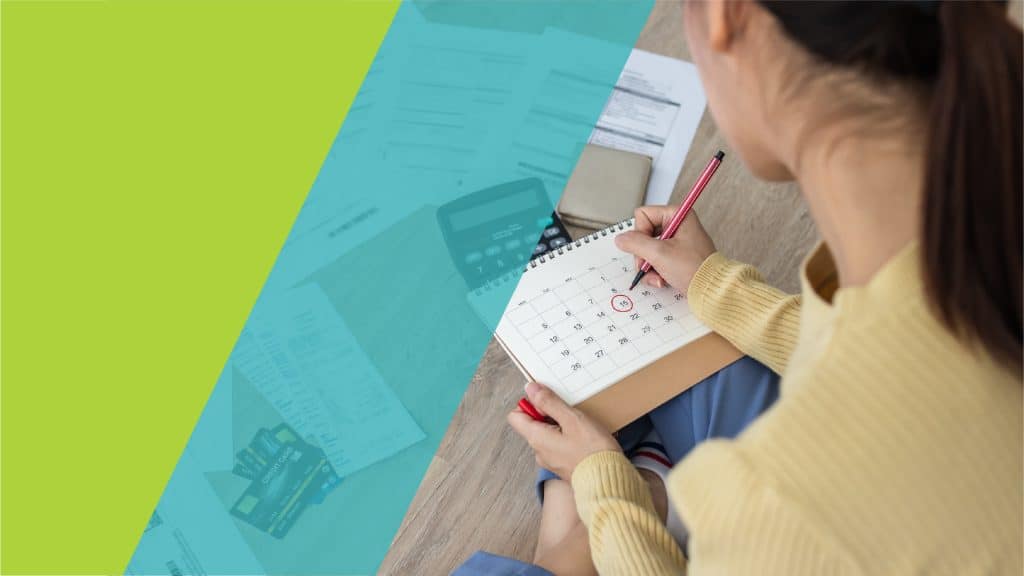Personne en train de marquer une date importante sur un calendrier, avec des documents et une calculatrice en arrière-plan.
