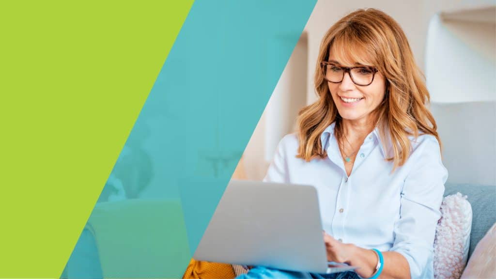 Une femme souriante travaille sur son ordinateur portable, assise confortablement dans un salon.