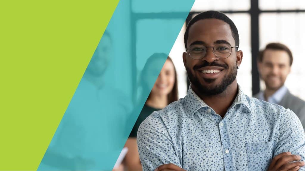 Un groupe de professionnels souriants dans un environnement de travail moderne, avec un focus sur une personne en premier plan, un homme avec des lunettes, vêtu d'une chemise à motifs.