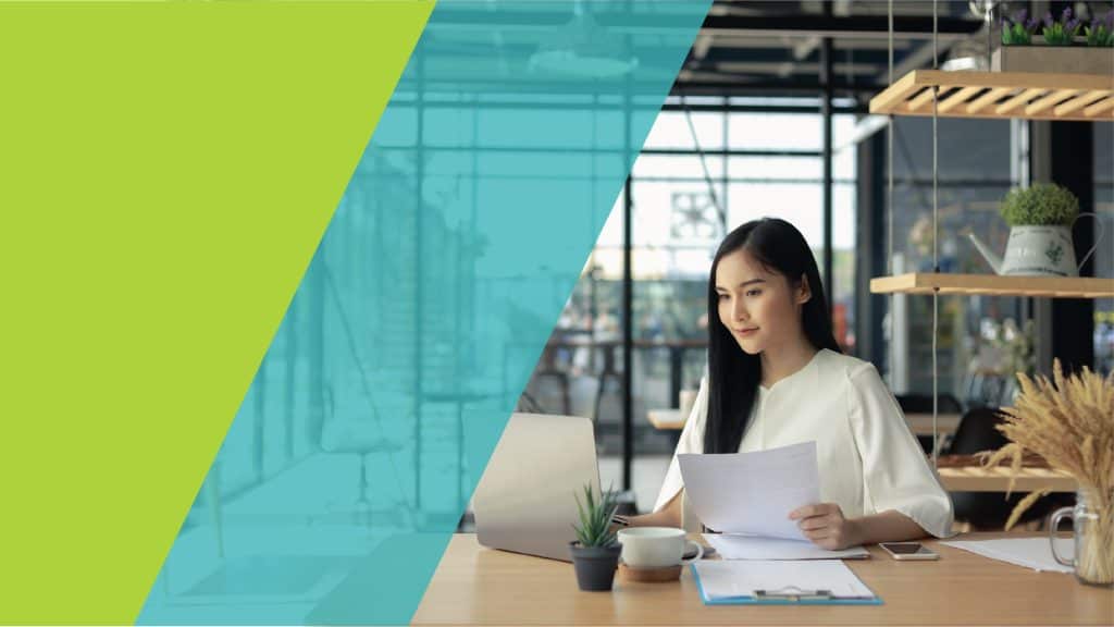 Une femme travaillant sur un ordinateur portable, tenant des documents dans ses mains, dans un environnement de bureau moderne.