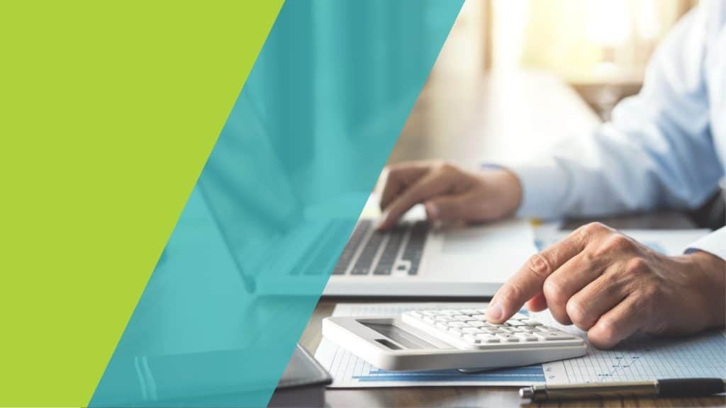 Un professionnel utilise une calculatrice tout en travaillant sur un ordinateur portable, avec des documents financiers devant lui.