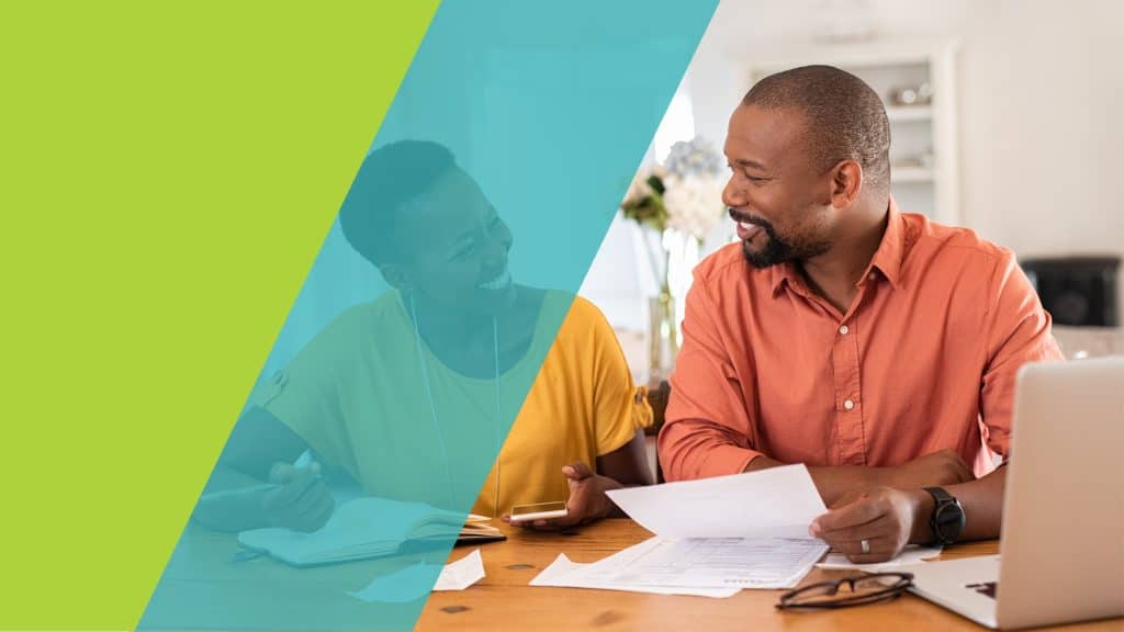 Un couple souriant examine des documents financiers ensemble à la maison, avec un ordinateur portable et un téléphone portable sur la table.
