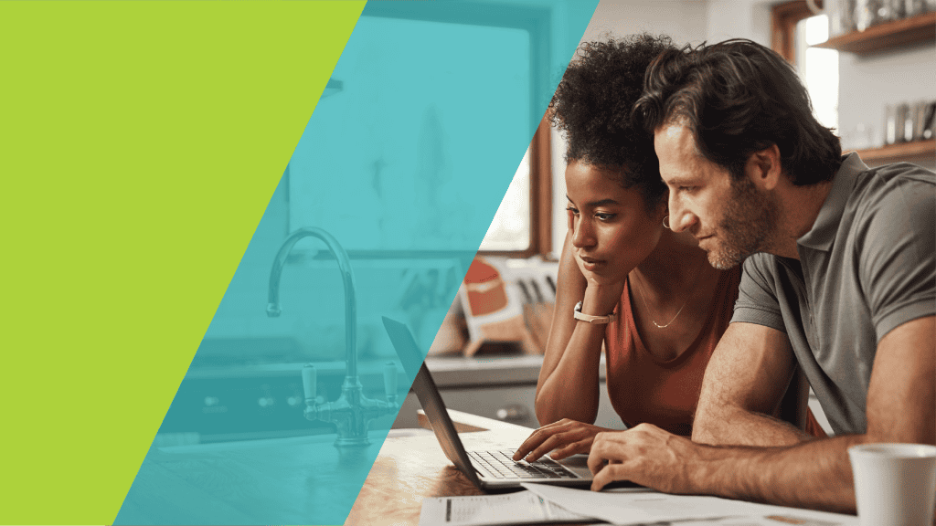 Couple concentré devant un ordinateur portable dans une cuisine, avec des documents posés sur la table