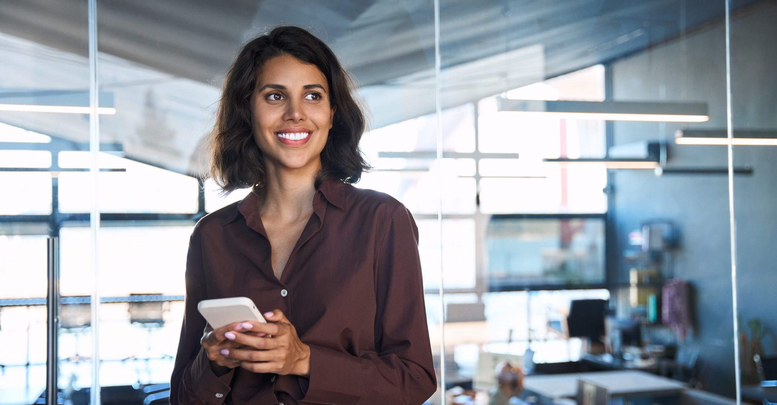 Mandataire souriante dans un bureau moderne tenant un smartphone.